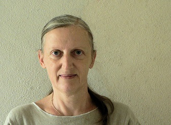 A portrait of a woman with long hair, wearing a light-colored dress, against a neutral background.