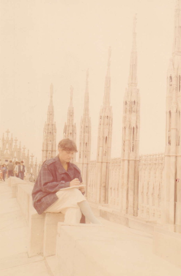 A person sitting on a ledge, sketching while surrounded by gothic architecture, with spires and ornate details in the background.