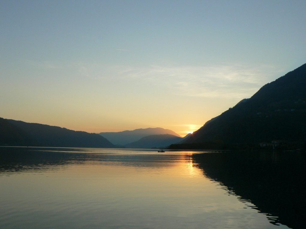 A serene landscape showcasing a calm lake at sunset, with mountains silhouetted against the sky.